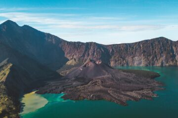 Stunning aerial view of a volcanic island surrounded by blue waters and rugged mountains.
