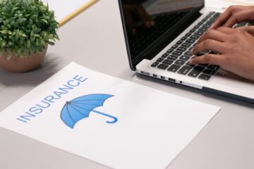 Close-up of hands typing on laptop with an insurance document visible on the desk.